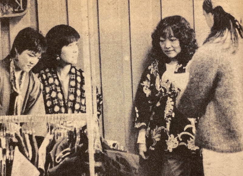 Four Asian women are gathered indoors, engaging in conversation and standing in front of a clothing rack