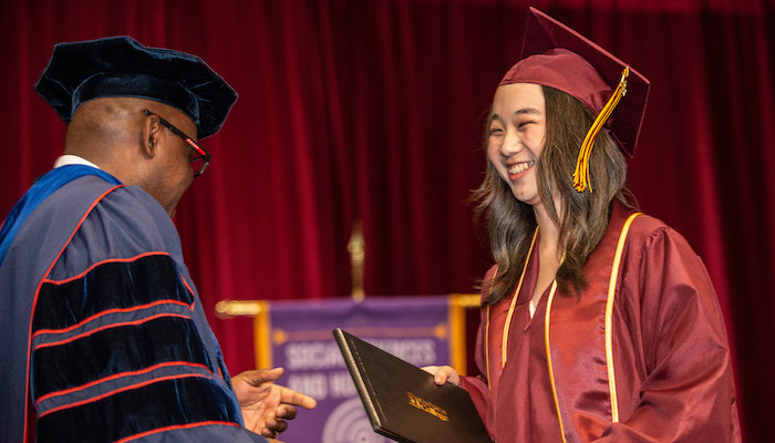Smiling graduate receiving diploma from President Holmes