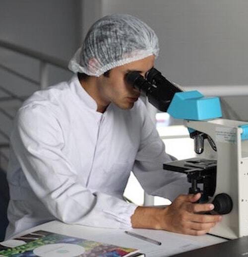 student in white lab coat looking into microscope