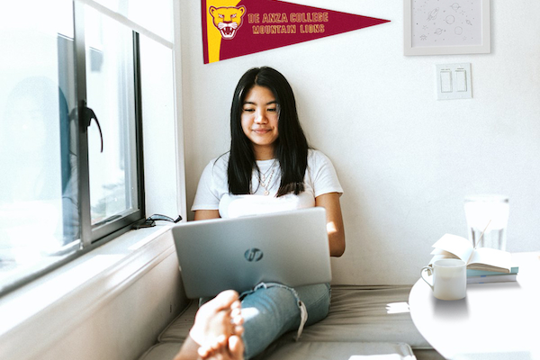 female student sitting on floor with laptop under a De Anza pennant